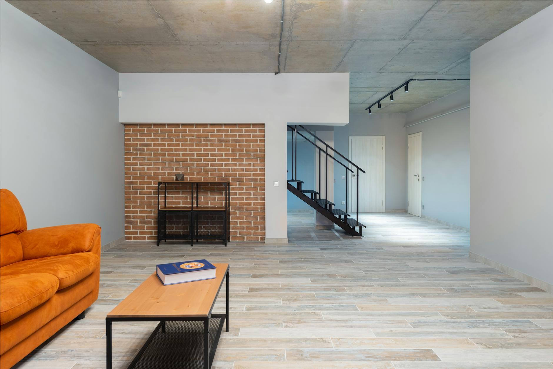 Pomarańczowa sofa w loftowym salonie z ceglaną ścianą i schodami